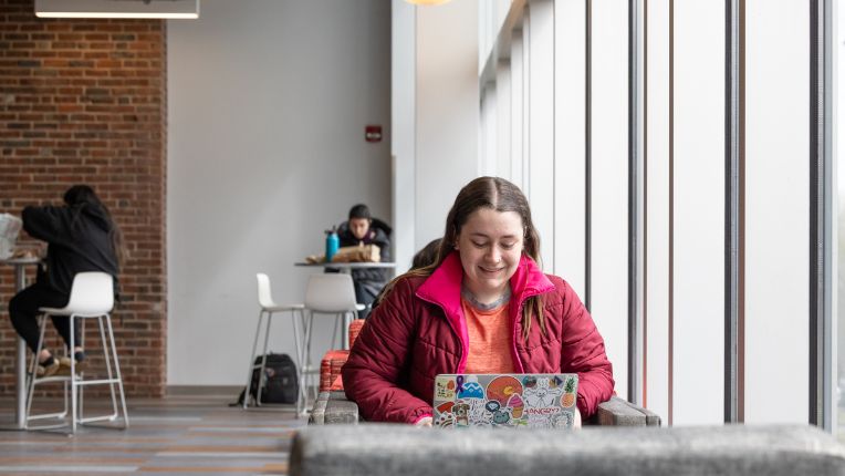A female student completing the common application from her laptop. She is smiling at her screen.
