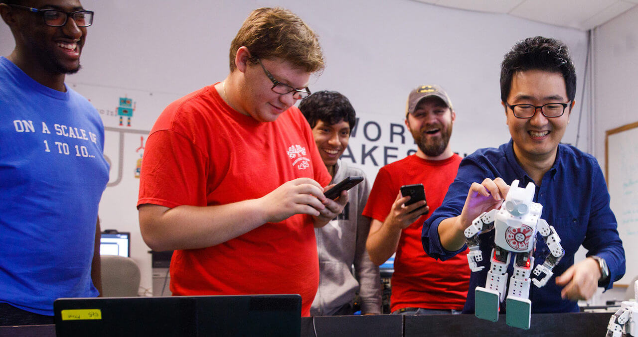 Students holding controls and a robotic character