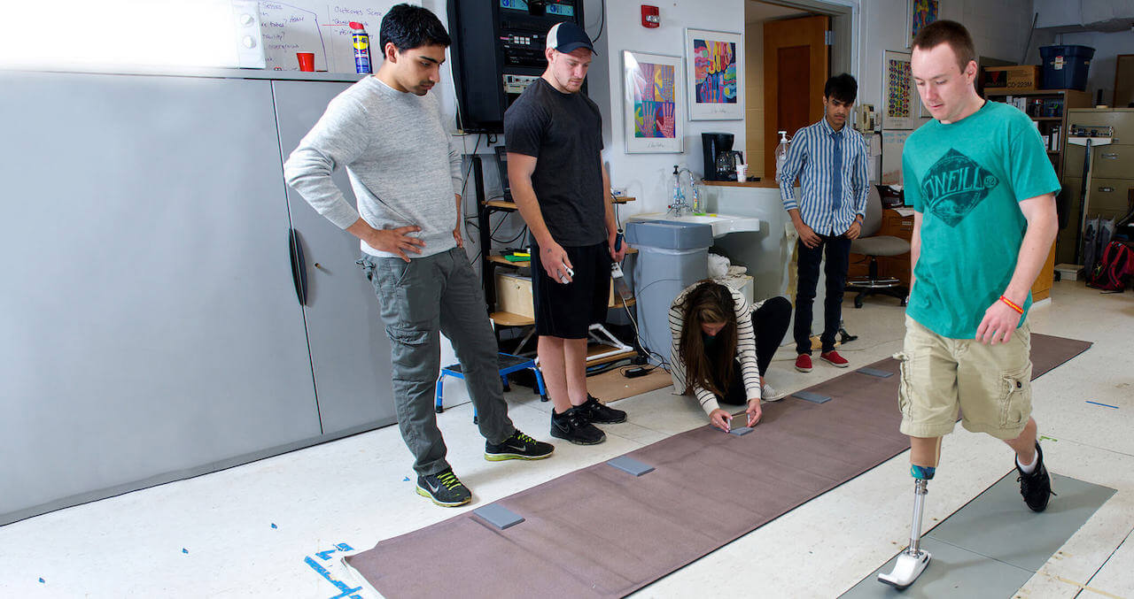 Students watch a man walk on a prosthetic leg