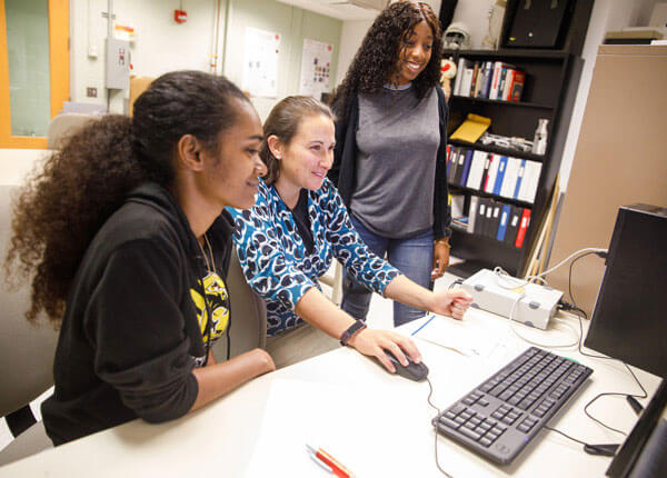 two female students with faculty member working on computer