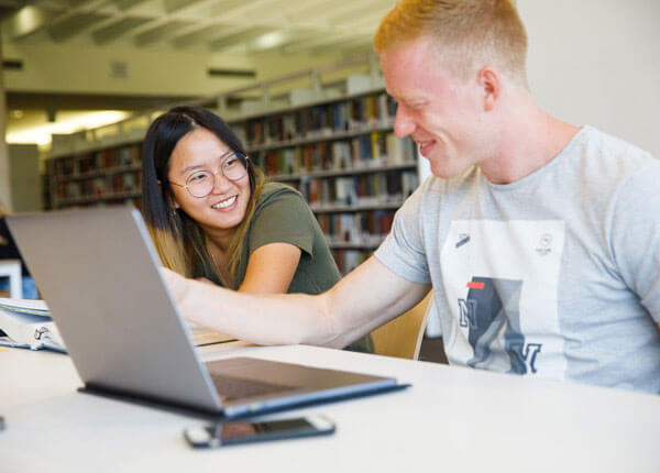 Two University of Hartford students smiling in the Mortensen Library.
