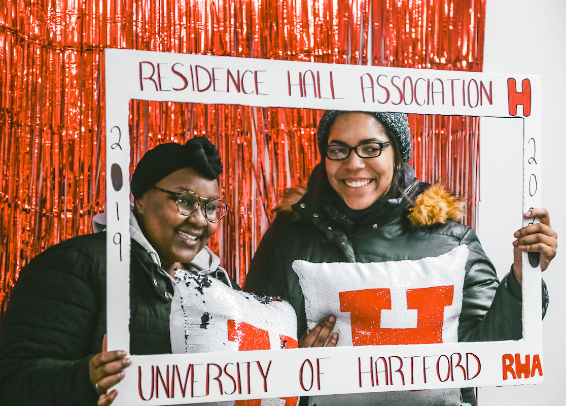 Image is of two students holding up a sign that says residence hall association