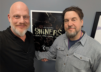 Seth McClellan and Bob Martin pose for the camera in front of their documentary poster.