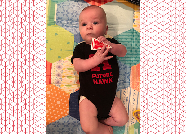 baby in uhart onesie holding a uhart pennant