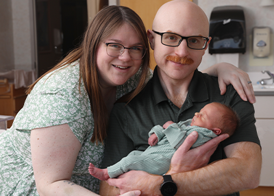 Sarah Carlyle Laskey and her husband smiling holding their new baby. 