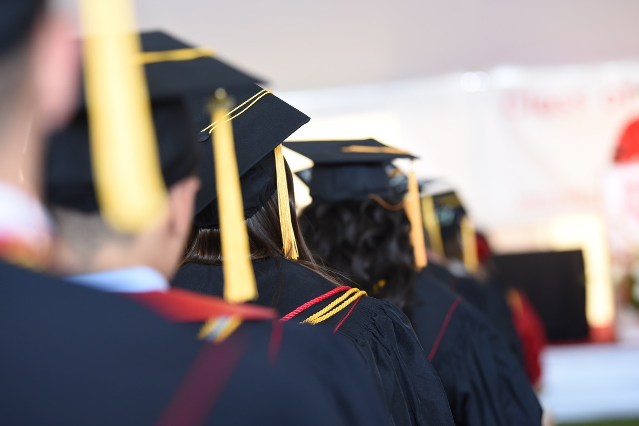 Image is of a line of students sitting at commencement with a view of their graduation caps