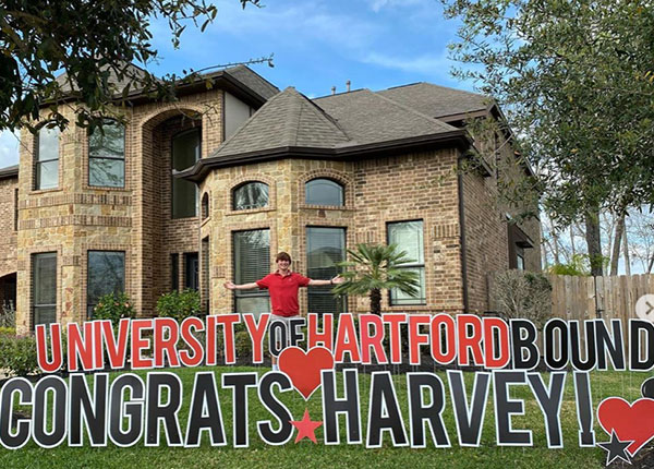Accepted Student in front of home, with sign University of Hartford bound