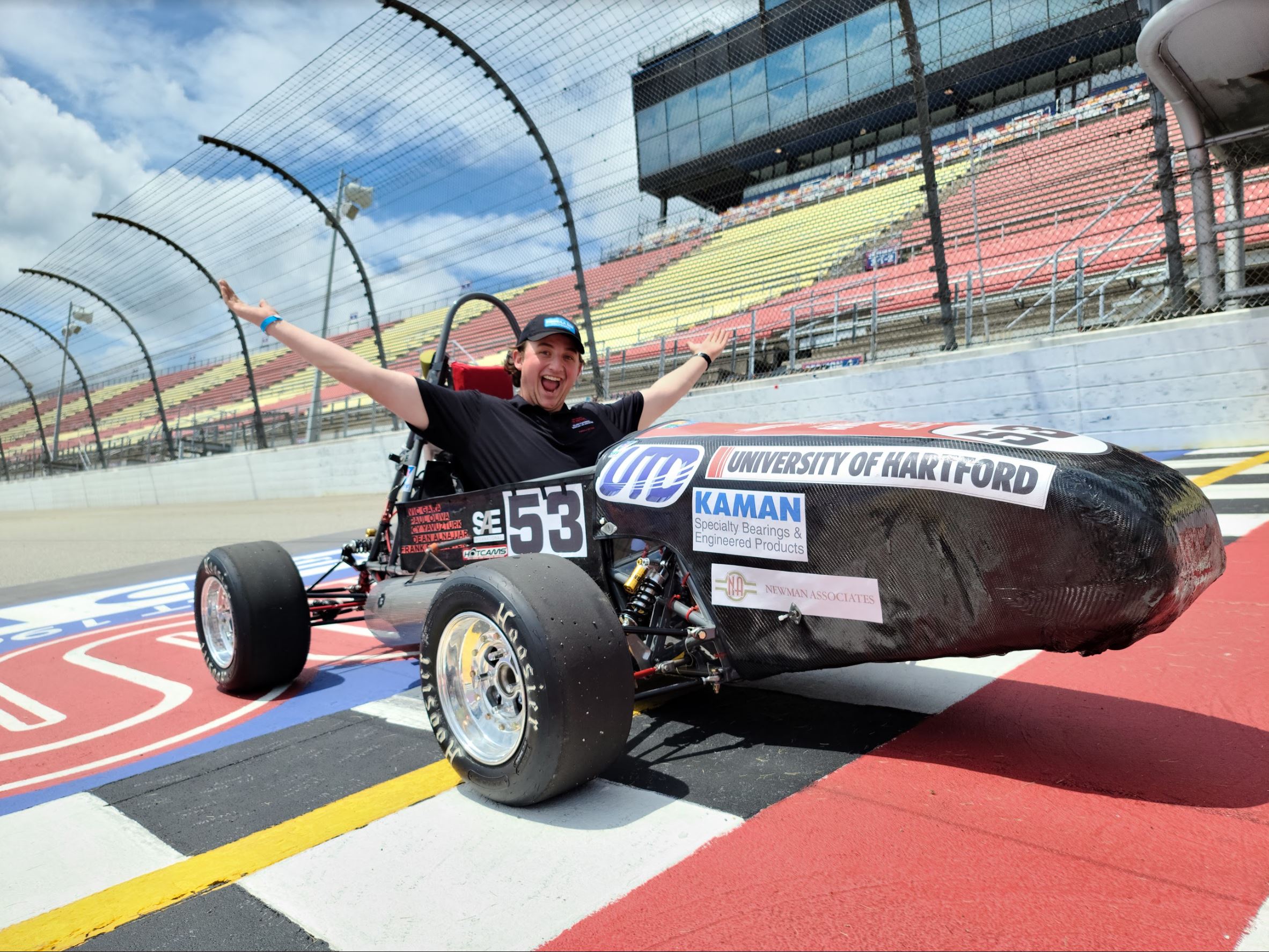 Male student in race car smiling with hands open.